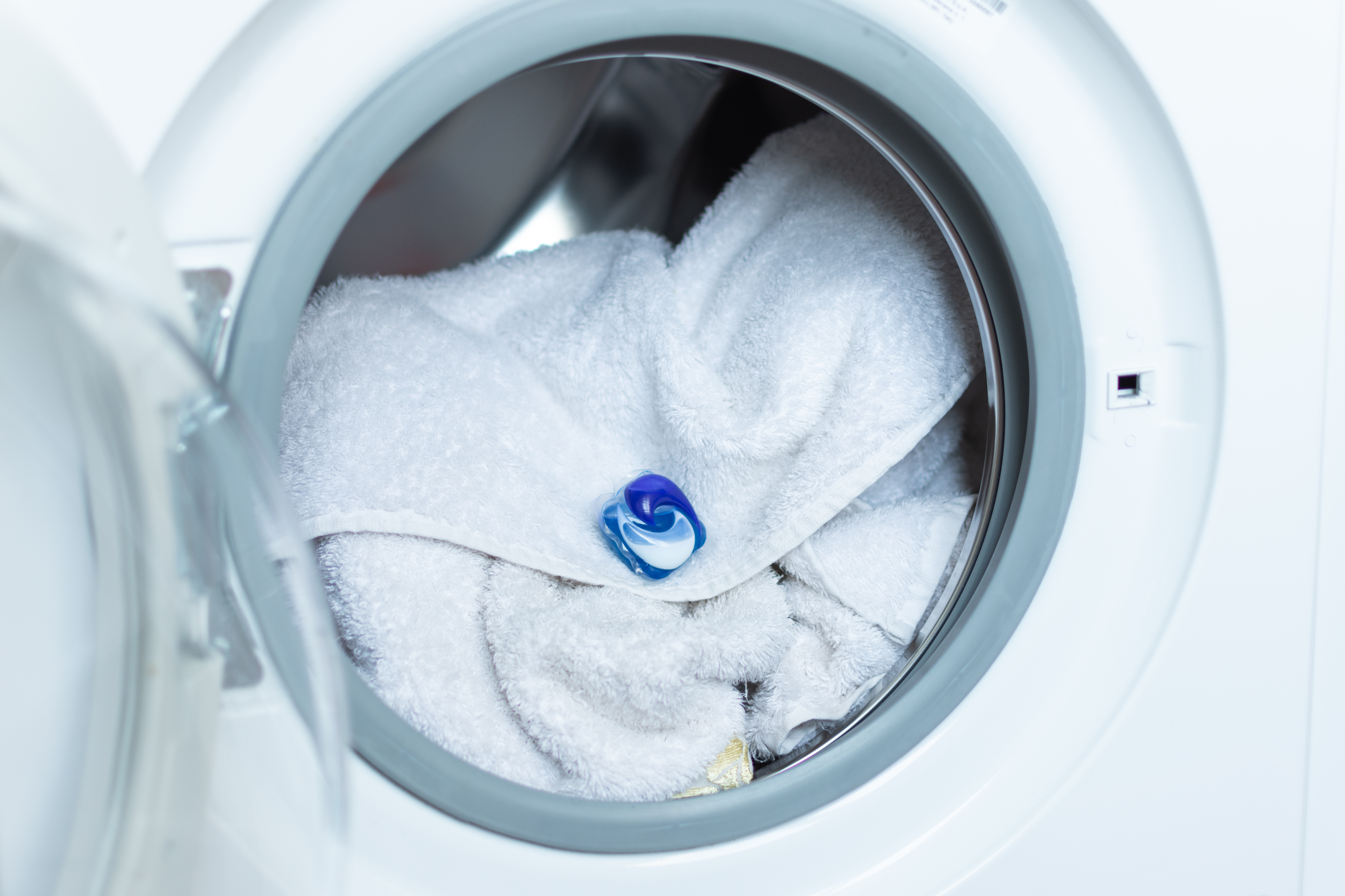 Laundry tablet in washing machine on top of white towels